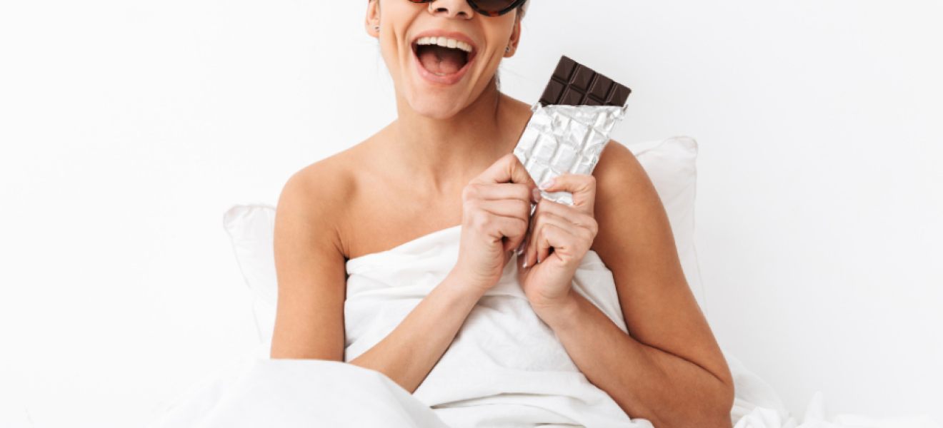 picture of a happy woman in a towel wearing sunglasses eating chocolate