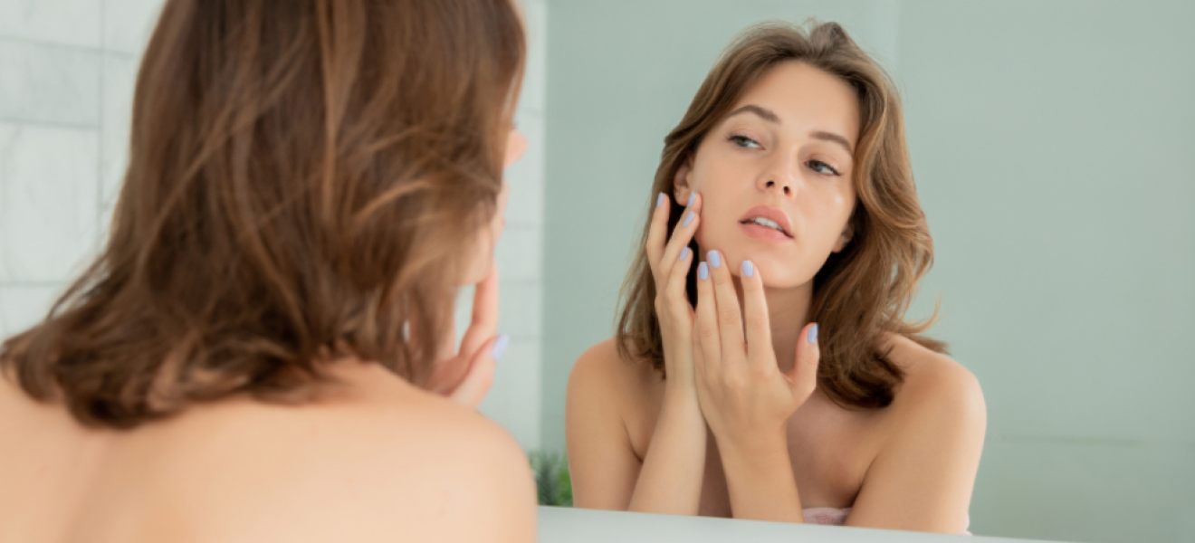 picture of a woman looking at her stressed skin in the mirror