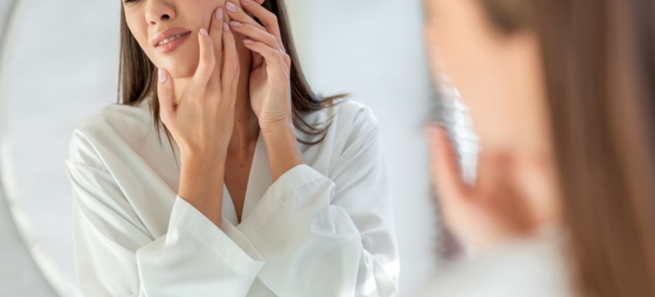 a woman frowning looking at herself in the mirror with some skin issues picture of a woman frowning looking at herself in the mirror with some skin issues
