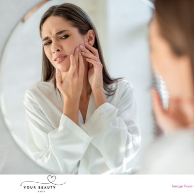 picture of a woman frowning looking at herself in the mirror with some skin issues